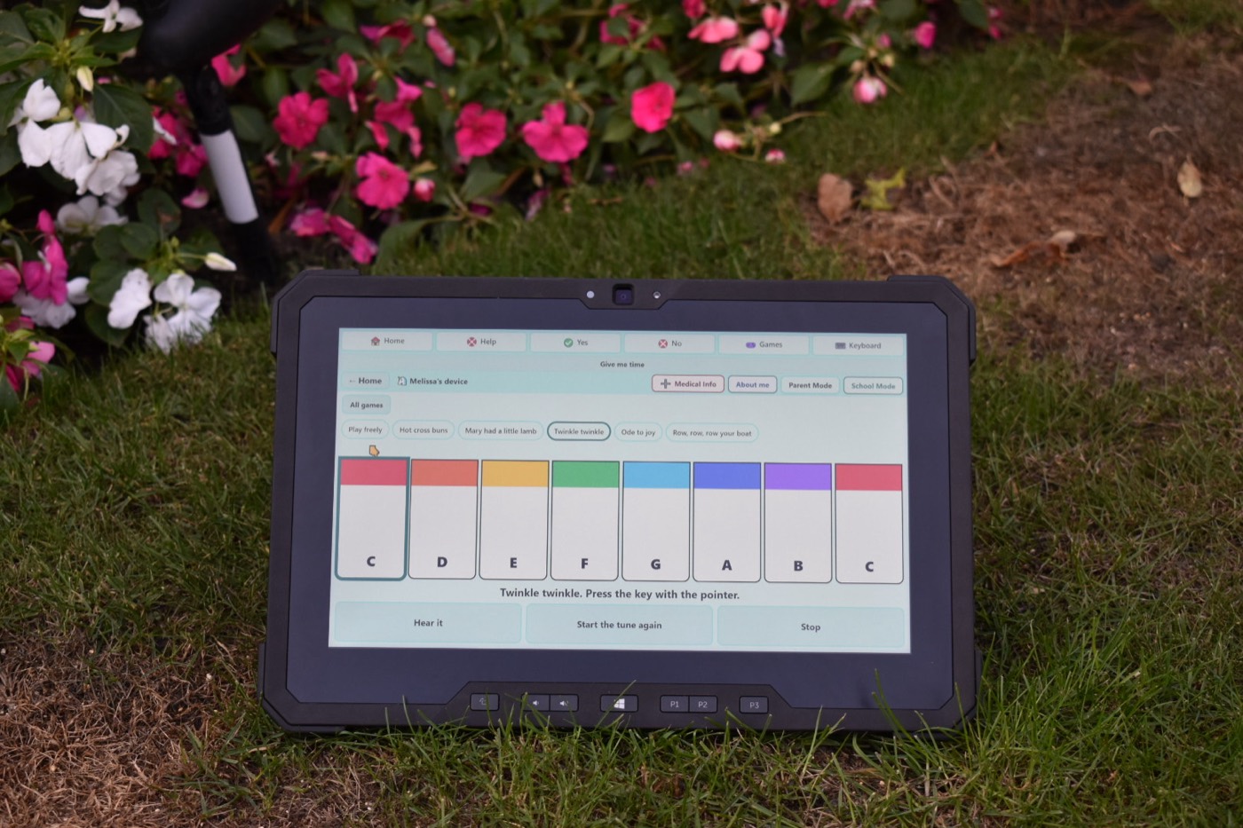 A Dell Latitude 7212 rugged tablet propped up in a flower bed, running the Piano game, with its P1, P2 and P3 buttons visible below the screen